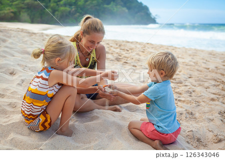 Happy kids with mother have fun on white sand beach. Couple of children playing with mother. Travel lifestyle, swimming activities in family summer camp. Vacations on tropical island. 126343046
