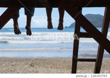 Happy kids have fun on beach walk. Children sit on lifeguard tower edge, dangling bare feet, look at sea surf. Black silhouette. Vacations travel lifestyle, outdoor activities in family summer camp. 126343703