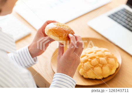 会社のデスクでパンを食べるミドル女性 会社のデスクでパンを食べるミドル女性 126343711