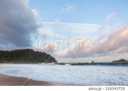 Amazing tropical beach with white sand, blue ocean waves, and lush greenery under a bright sky. Capturing the beauty of an untouched paradise and a perfect vacation escape. 126343729