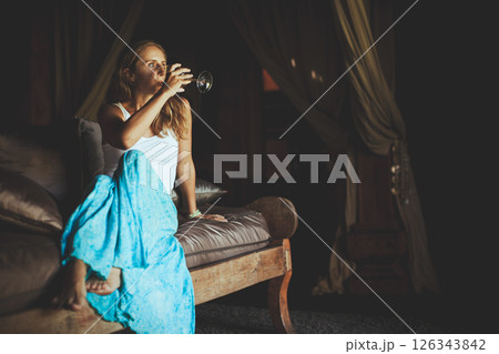 Young woman sit on sofa inside luxury wooden villa. Girl relaxing on family summer vacation. Tropical lifestyle. 126343842