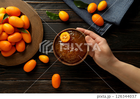 Fresh kumquat fruits on wooden plate and bowl with jam in hand on wooden background, top view Fresh kumquat fruits on wooden plate and bowl with jam in hand on wooden background, top view 126344037