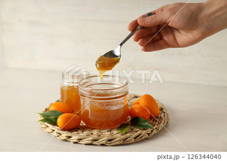 Kumquat fruits, jars with jam  and spoon in hand on light background 126344040
