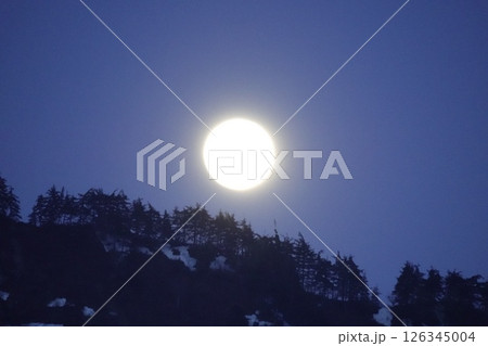 雪渓残る山の稜線の月と木立のシルエット 126345004
