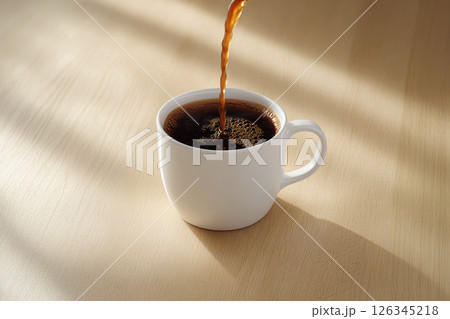 Close-up of hot black coffee being poured into a white cup on a wooden surface. 126345218