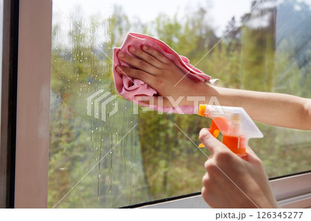 Cleaning windows with a spray cleaner and a napkin on a sunny day in a cozy room Cleaning windows with a spray cleaner and a napkin on a sunny day in a cozy room 126345277