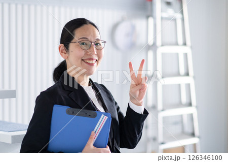 笑顔でワンポイントサインをする女性建築士 126346100