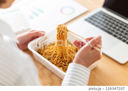 会社のデスクでインスタント焼きそばを食べながら働くミドル女性 126347287