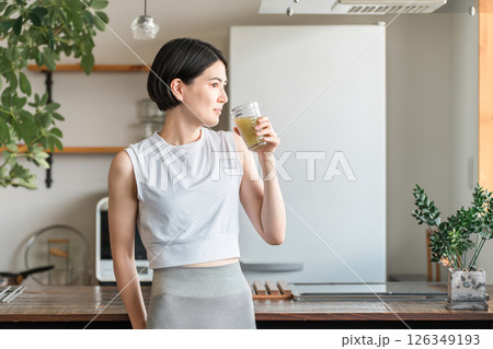 家・自宅のリビングでトレーニング後に水分補給,栄養補給する若いアジア人女性 126349193