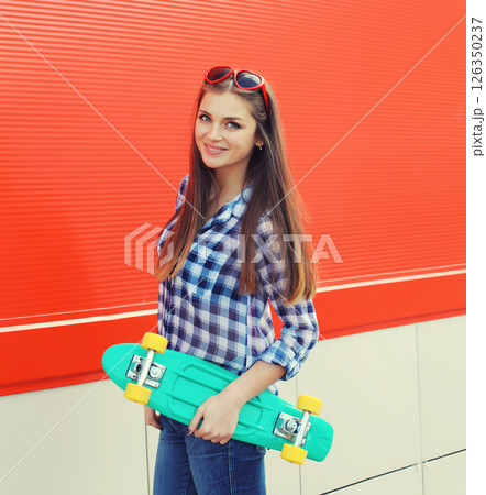 Summer portrait of happy cheerful stylish young woman with skateboard posing on red background Summer portrait of happy cheerful stylish young woman with skateboard posing on red background 126350237