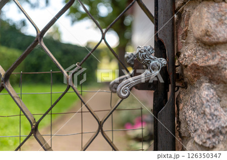 An ornate metal gate handle opens to a lush garden pathway on a sunny day in summer An ornate metal gate handle opens to a lush garden pathway on a sunny day in summer 126350347