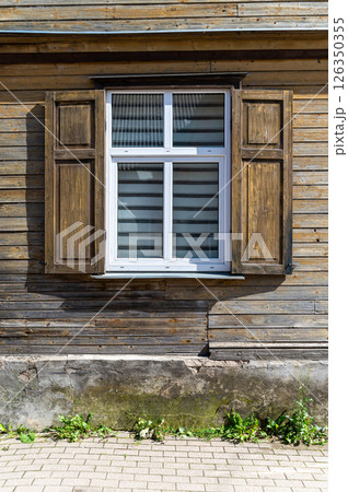 A wooden window with shutters opens to a rustic exterior of a house on a sunny day A wooden window with shutters opens to a rustic exterior of a house on a sunny day 126350355