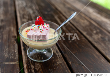 Dessert served in a glass bowl featuring a slice of pink mousse topped with a strawberry on a wooden table Dessert served in a glass bowl featuring a slice of pink mousse topped with a strawberry on a wooden table 126350588