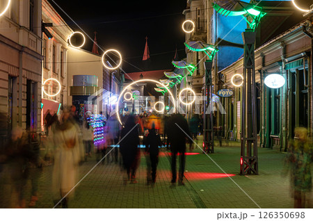 People walk through a brightly lit street at night 126350698