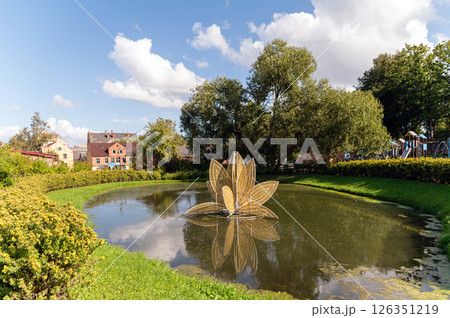 A peaceful pond features a lotus fountain amid lush greenery on a sunny day. A peaceful pond features a lotus fountain amid lush greenery on a sunny day. 126351219