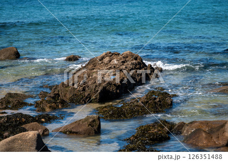 Rocky shoreline with gentle waves lapping against boulders on a sunny day 126351488