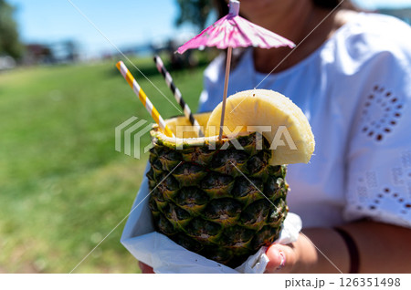Refreshing tropical drink served in a pineapple with umbrellas and fruit garnish outside Refreshing tropical drink served in a pineapple with umbrellas and fruit garnish outside 126351498