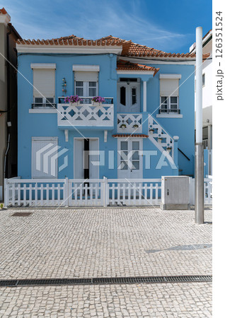 Bright blue beach house with balcony and white fence in a coastal town under clear sky Bright blue beach house with balcony and white fence in a coastal town under clear sky 126351524