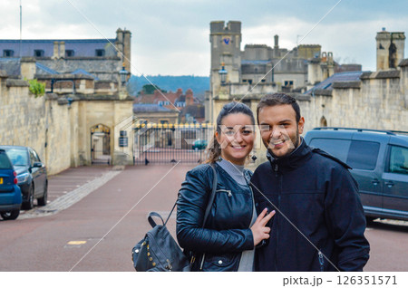 Smiling couple standing in front of Windsor Castle in England, captured on a cloudy day visit to the royal landmark, enjoying their travel experience Smiling couple standing in front of Windsor Castle in England, captured on a cloudy day visit to the royal landmark, enjoying their travel experience 126351571