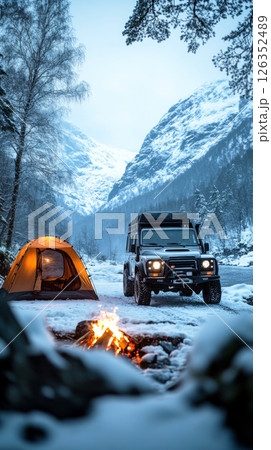 Firelight glows as lone camper faces cold night beside off-road truck and tent, braving deep snow and fierce wind in a bold wild camp adventure 126352489
