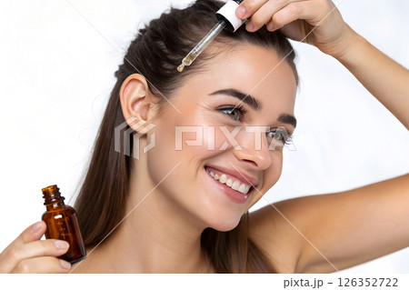 woman applying hair serum with pipette to scalp, haircare treatment with essential oil droplet, therapeutic hair restoration product application with glass dropper 126352722