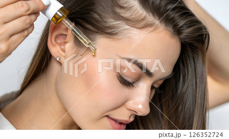 woman applying hair serum with pipette to scalp, haircare treatment with essential oil droplet, therapeutic hair restoration product application with glass dropper 126352724
