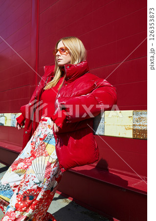 High fashion photo of a young blond woman in red glossy down jacket, poloneck, and pants. Monochrome trendy red outfit. High fashion photo of a young blond woman in red glossy down jacket, poloneck, and pants. Monochrome trendy red outfit. 126353873