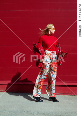 High fashion photo of a young blond woman in red glossy down jacket, poloneck, and pants. Monochrome trendy red outfit. High fashion photo of a young blond woman in red glossy down jacket, poloneck, and pants. Monochrome trendy red outfit. 126353878