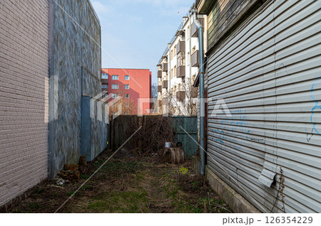 Narrow alleyway between buildings with overgrown vegetation and distant residential view 126354229