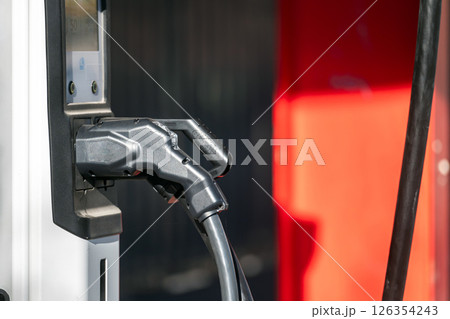 An electric vehicle connects to a charger in a bustling city during bright daylight. 126354243