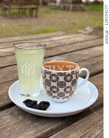 Traditional Turkish coffee served with lemon water and raisins on white saucer over rustic wooden table 126354277