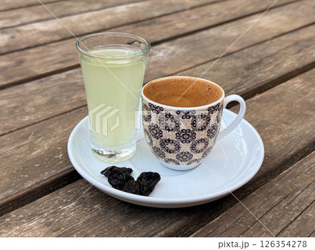 Traditional Turkish coffee served with lemon water and raisins on white saucer over rustic wooden table 126354278