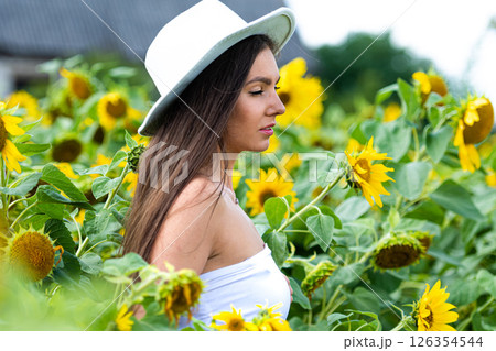beautiful woman posing in a field of sunflowers in a white top and hat at sunny day beautiful woman posing in a field of sunflowers in a white top and hat at sunny day 126354544