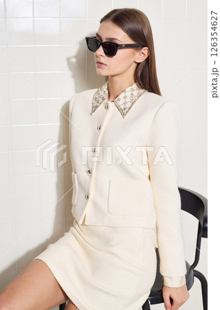 Stylish female fashion model poses confidently in a trendy beige outfit and sunglasses indoors Stylish female fashion model poses confidently in a trendy beige outfit and sunglasses indoors 126354627