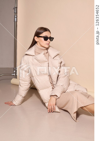 beautiful fashion female model in beige down jacket and long wool turtleneck dress in studio. beautiful fashion female model in beige down jacket and long wool turtleneck dress in studio. 126354652