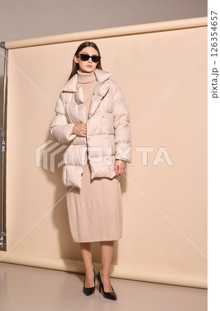 beautiful fashion female model in beige down jacket and long wool turtleneck dress in studio. beautiful fashion female model in beige down jacket and long wool turtleneck dress in studio. 126354657