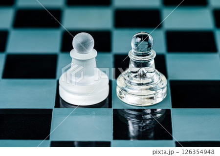 two opponent glass chess pawns on a glass chess board, black background 126354948