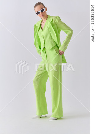 High fashion portrait of young confident female model in green lime color three-piece suit. Monochrome green outfit High fashion portrait of young confident female model in green lime color three-piece suit. Monochrome green outfit 126355614