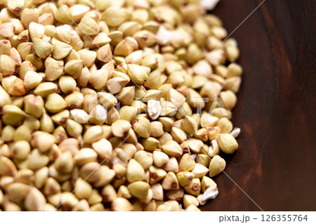 Raw buckwheat grains in brown wooden bowl. Uncooked organic dried ingredient. Macro shot. Top view.  126355764