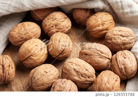 Pile of whole unshelled walnuts on wooden table with crumpled cloth napkin. Top view 126355788