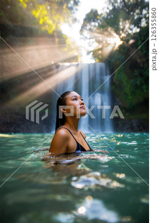 Serenity in Nature With a Woman Enjoying a Tranquil Moment Near a Waterfall at Sunset 126355860