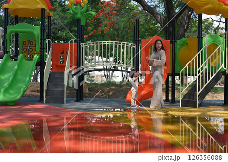 Mother and toddler exploring colorful playground after rain 126356088