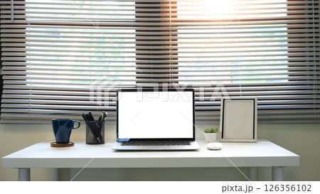 Contemporary home office desk with blank laptop screen in front of large window blinds Contemporary home office desk with blank laptop screen in front of large window blinds 126356102