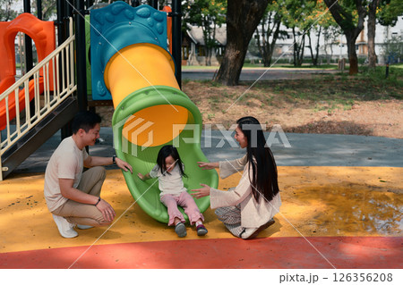 Joyful little girl enjoys sliding with support from her loving parents on both sides Joyful little girl enjoys sliding with support from her loving parents on both sides 126356208