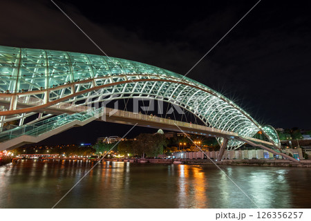 Peace bridge, steel and glass construction pedestrian bridge over Kura Mtkvari river in central Tbilisi, capital of Georgia 126356257