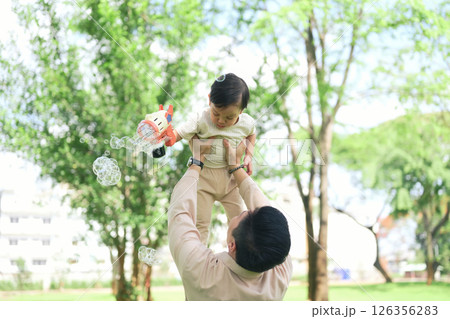 joyful dad lifts his toddler high in the air as the child holds a bubble gun 126356283