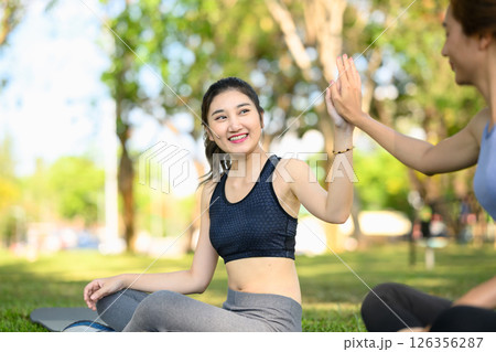 Two athletic women share a cheerful high-five after completing an outdoor workout in a green park. 126356287