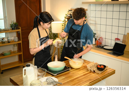 Happy couple preparing homemade pancakes in a warm kitchen Happy couple preparing homemade pancakes in a warm kitchen 126356314