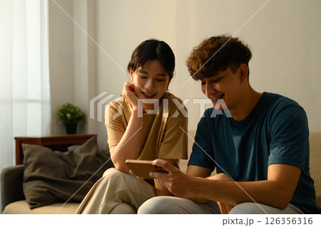 Couple enjoys browsing a smartphone together on sofa in their living space 126356316