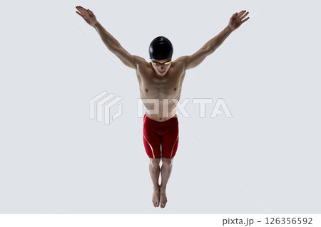 Athlete mid-jump in diving motion with raised arms and focused gaze against white background to emphasize form, grace and muscle control. Athlete mid-jump in diving motion with raised arms and focused gaze against white background to emphasize form, grace and muscle control. 126356592